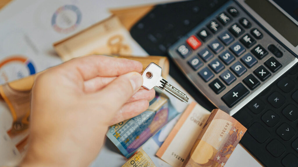 Hand holding a house key and a calculator on the background